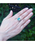 Emerald-cut men's emerald ring with side diamonds, bezel set in 18K white gold on a hand.