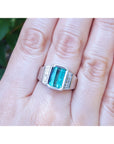 A men's emerald ring in white gold on a person's finger against a natural background.