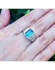 Men's 18K white gold ring with a bezel-set emerald-cut bluish-green emerald and side diamonds.
