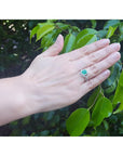 Emerald-cut natural emerald ring with halo diamonds on an 18K white gold band, worn on a hand.