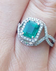 A square emerald ring with diamond accents on a finger.