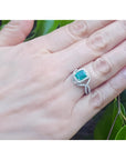 Emerald-cut natural emerald ring with halo diamonds on an 18K white gold split shank band.
