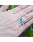 Emerald-cut natural emerald ring with halo diamonds on an 18K white gold split shank band.