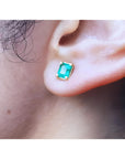 Emerald-cut natural emerald stud earring in 14K yellow gold, worn on an ear.