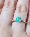 1.13 carat emerald-cut Muzo Colombian emerald set in a simple gold ring on a hand.