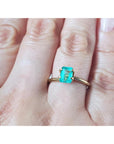 1.13 carat emerald-cut Muzo Colombian emerald set in a simple gold ring on a hand.