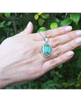 Emerald-cut Colombian emerald pendant with natural diamonds in 14K white gold, held on a hand.