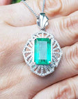On a hand being displayed a natural emerald pendant with accent diamonds crafted in white gold.