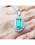 On a hand being displayed a natural emerald pendant with accent diamonds crafted in white gold.