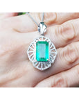 Emerald-cut emerald pendant with natural diamonds in 14K white gold, held by a hand.