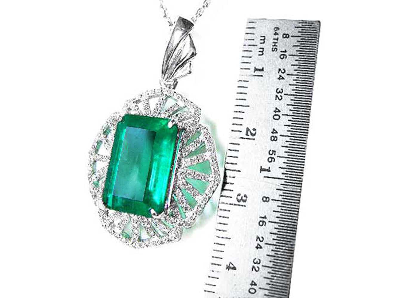 Emerald green gemstone pendant with white gold chain, next to a ruler for scale.