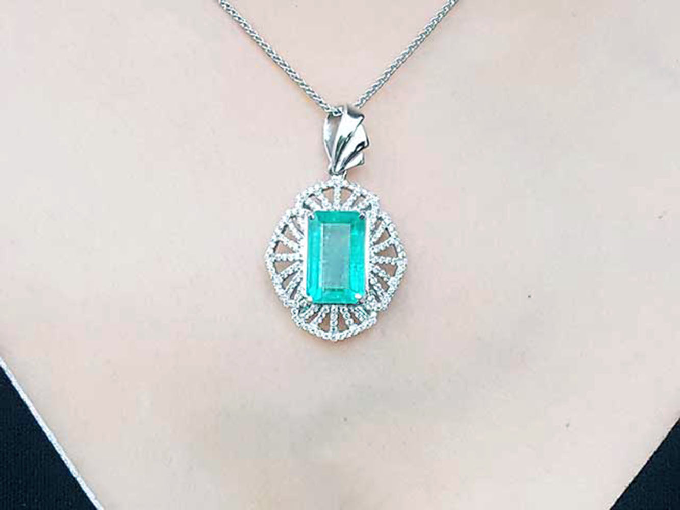 A rectangular natural emerald pendant in white gold and accent diamonds on topside view.