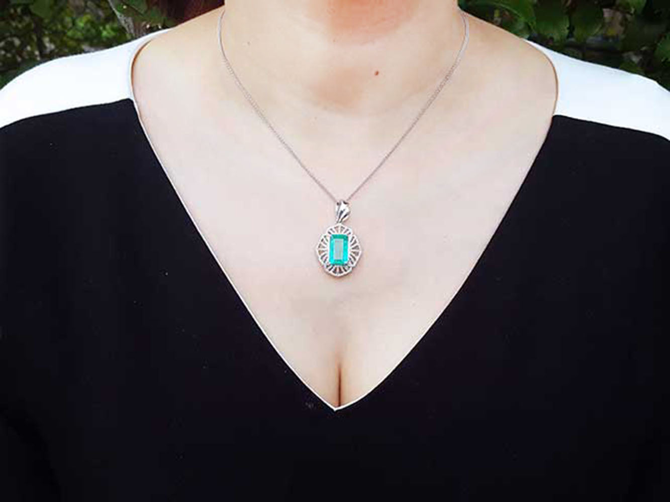 A woman wearing a black top with a necklace featuring a natural emerald-cut emerald pendant.
