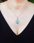 A woman wearing a black top with a necklace featuring a natural emerald-cut emerald pendant.