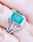 A close-up of an emerald ring with three rows of diamond accents on a hand.