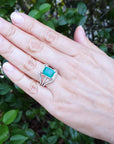 Hand wearing an emerald ring with a leafy background