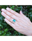 Hand wearing an emerald ring with a leafy background