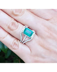 Emerald-cut 3.90 ct natural emerald ring with triple diamond rows on 14K white gold, worn on a hand.