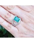 Emerald-cut 3.90 ct natural emerald ring with triple diamond rows on 14K white gold, worn on a hand.