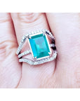 Women's emerald ring in 14k white gold with three rows of natural diamonds on a finger.