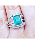 Women's emerald ring in 14k white gold with three rows of natural diamonds on a finger.