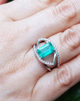 Close-up of a white gold emerald and diamond ring on a hand.
