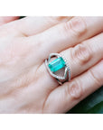 Rectangular emerald-cut emerald ring with diamond split shank in 14K white gold on a hand.