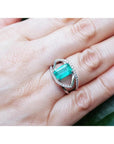 Rectangular emerald-cut emerald ring with diamond split shank in 14K white gold on a hand.