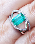 A close-up of a rectangular emerald ring white gold with diamonds on a finger.