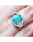 A close-up of a rectangular emerald ring white gold with diamonds on a finger.