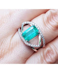 Rectangular emerald-cut emerald ring with diamond double halo and split shank in 14K white gold.