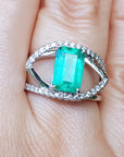Ring with a rectangular emerald and split shank with diamonds on a finger.