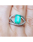Ring with a rectangular emerald and split shank with diamonds on a finger.