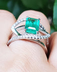 White gold ring with diamonds a top Colombian emerald on a finger against a natural background.