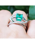 White gold ring with diamonds a top Colombian emerald on a finger against a natural background.