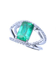 A white gold split shank ring with diamonds and a natural emerald on top.