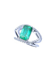 A white gold split shank ring with diamonds and a natural emerald on top.