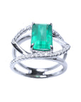 A white gold ring with a rectangular emerald on split shank with diamonds.