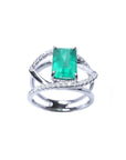 A white gold ring with a rectangular emerald on split shank with diamonds.