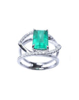 Emerald-cut emerald ring in 14K white gold with split shank and double row of diamonds.