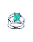 Emerald-cut emerald ring in 14K white gold with split shank and double row of diamonds.