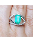 14k white gold ring with a rectangular emerald and split shank with natural diamonds on a finger.