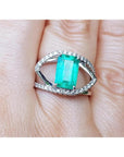 14k white gold ring with a rectangular emerald and split shank with natural diamonds on a finger.