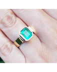 Emerald-cut 2.05 ct. emerald solitaire ring, bezel set in high polish 14K gold on a hand.