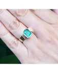 Emerald-cut emerald solitaire ring, bezel set in high polish 14K gold, worn on a hand.