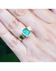 Emerald-cut emerald solitaire ring, bezel set in high polish 14K gold, worn on a hand.