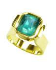 A solitaire emerald ring in yellow gold for women showing the top bezel set of the gem.