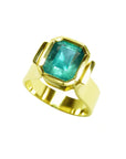 A solitaire colombian emerald ring for women in 14k yellow gold bezel set emerald-cut.