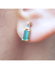 Natural baguette cut colombian emerald and diamond stud earrings worn on an ear.