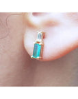 Natural baguette cut colombian emerald and diamond stud earrings worn on an ear.